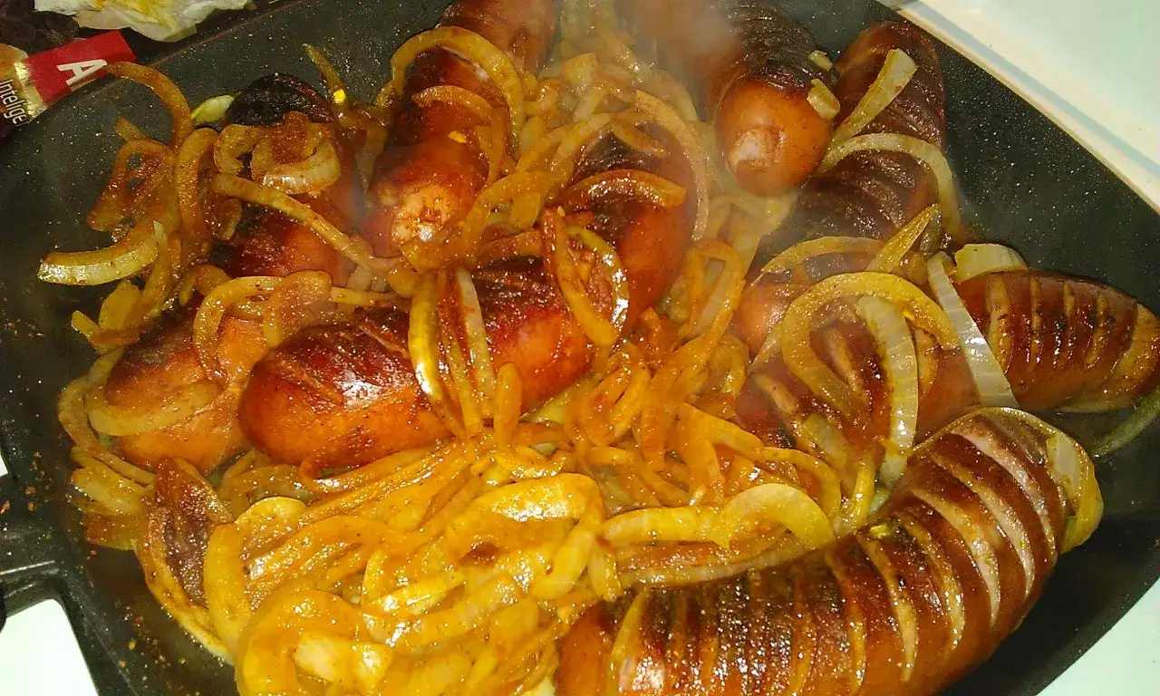 Smażona kiełbasa z cebulą na patelni. Złociste, rumiane kiełbaski i karmelizowana cebulka. Idealny sposób, by dowiedzieć się, ile smażyć kiełbasę na patelni.