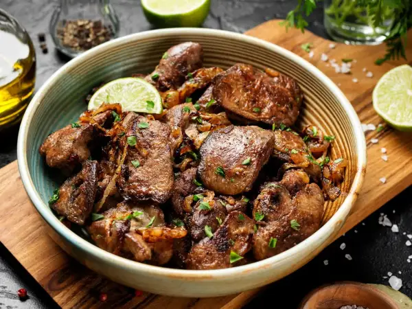 Miseczka z duszonymi kawałkami wątróbki, ozdobiona plasterkiem limonki i posypana natką pietruszki.