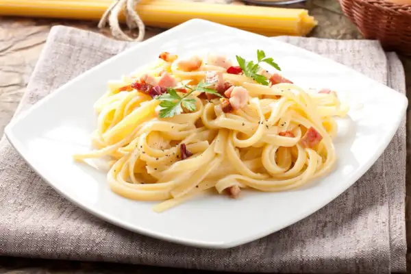 Pyszne spaghetti carbonara, przygotowane według oryginalnego przepisu, z chrupiącym boczkiem i świeżą natką pietruszki.