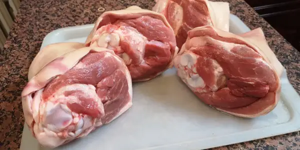 Surowe golonki wieprzowe na tacy, gotowe, by dowiedzieć się, ile piec golonkę w piekarniku.