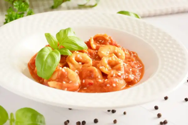 Pyszne tortellini w sosie pomidorowym, posypane sezamem i udekorowane listkami bazylii.