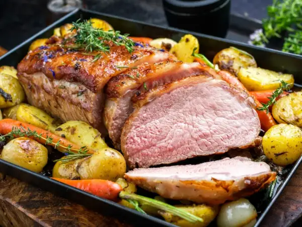 Soczysta polędwiczka wieprzowa pieczona w piekarniku z ziemniakami i marchewką, udekorowana ziołami.