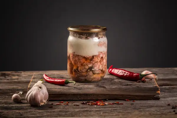Słoik z mięsnym sosem do spaghetti, obok papryczki chili i czosnku. Czy można zawekować sos do spaghetti z mięsem? Tak, to świetny sposób na jego przechowywanie.