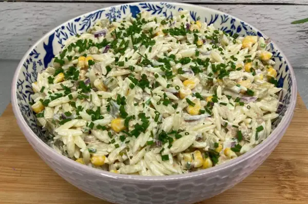Pyszna sałatka z tuńczykiem i makaronem orzo, z kukurydzą i szczypiorkiem, w ozdobnej misce.