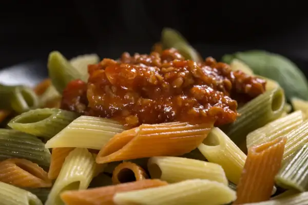 Kolorowy makaron penne z sosem bolońskim. Dowiedz się, jak dobrać sos do makaronu spaghetti a penne, zasady przywierania.