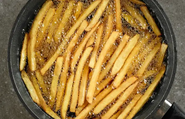 Smażone frytki w gorącym oleju. Aby uniknąć nasiąkania frytek tłuszczem, kluczowe jest utrzymanie wysokiej temperatury oleju.