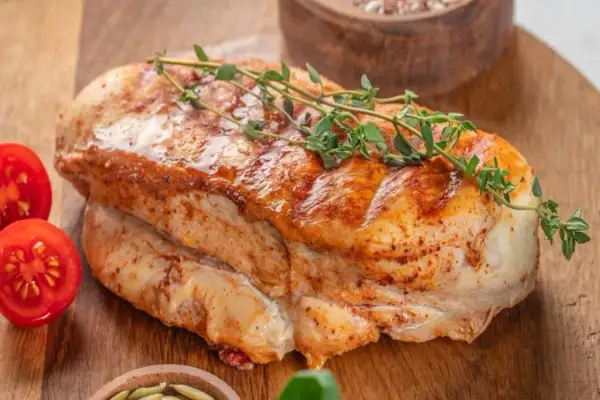 Soczysty filet z indyka duszony, z gałązką tymianku i pomidorkami koktajlowymi na desce.