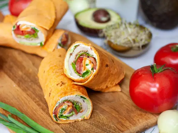 Pyszna tortilla z szynką, świeżymi warzywami i kremowym serkiem, ułożona na desce z dodatkami.